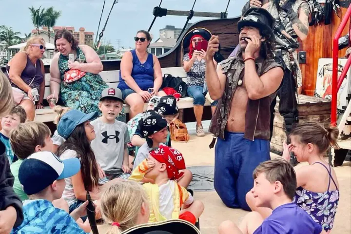 A group of children listen to a costumed pirate speaking on a boat deck.