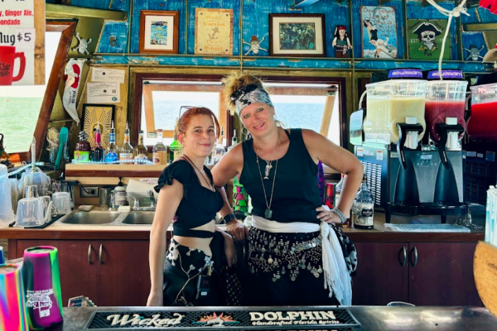 Two women behind a bar with colorful decor and drink machines.