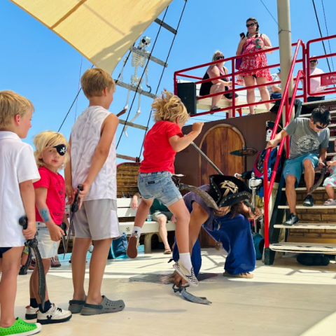 Children on a ship deck, dressed as pirates, watch an acrobatic performer in bright daylight.