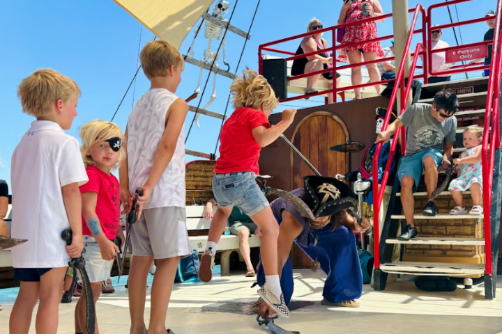 Children on a ship deck, dressed as pirates, watch an acrobatic performer in bright daylight.
