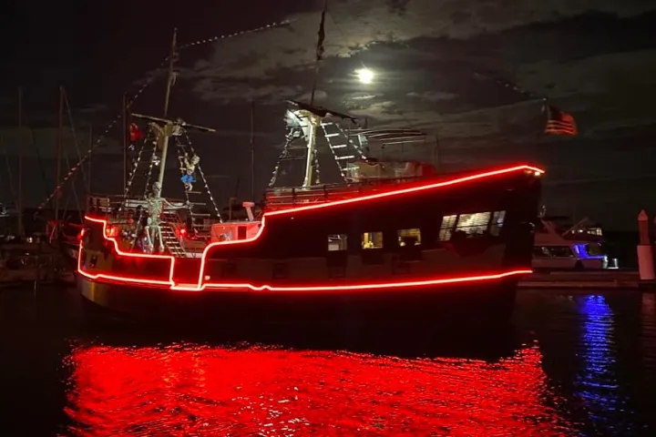 A ship with red lights glows on the water at night under a full moon.