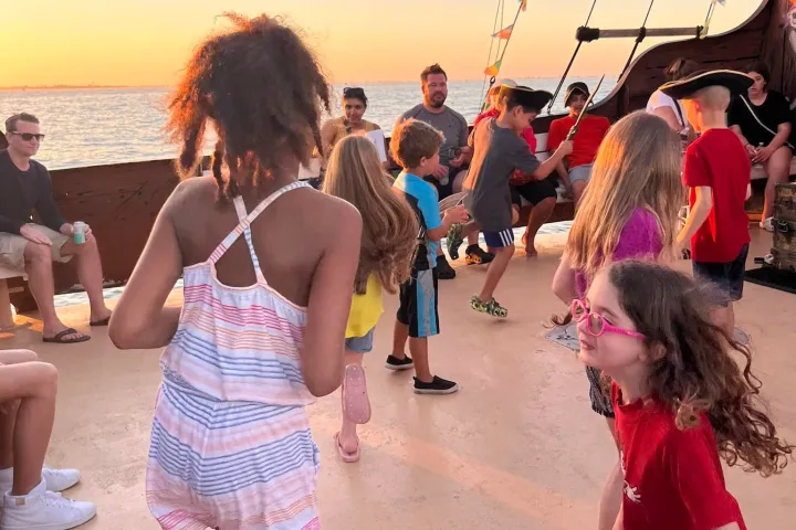 Children dancing on a ship deck at sunset with adults watching.