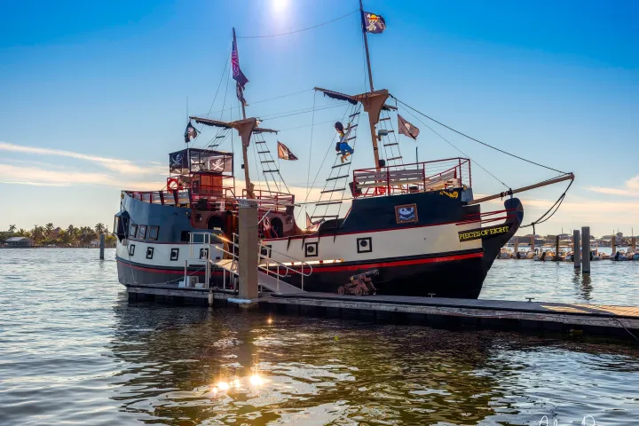 Pirate-themed ship docked at a marina under a clear blue sky, sunlight reflecting on water.
