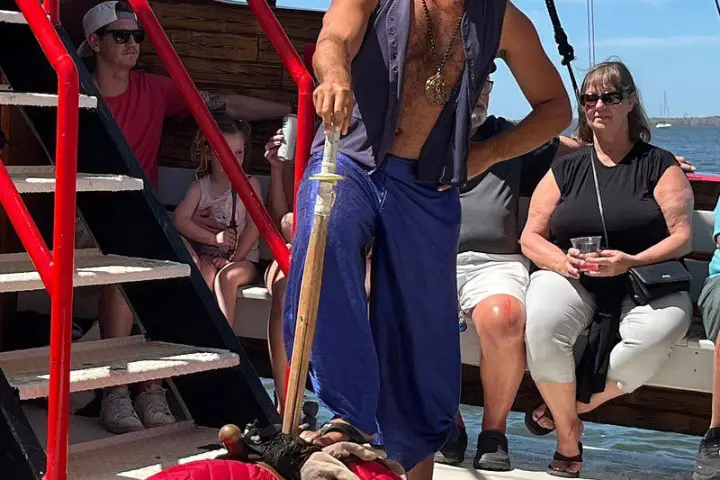 Two people in pirate costumes on a ship deck with an audience watching.