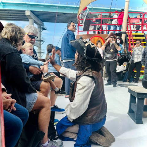 Pirate high-fives a child on a ship with people gathered around on a sunny day.