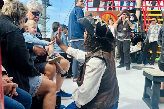 Pirate high-fives a child on a ship with people gathered around on a sunny day.