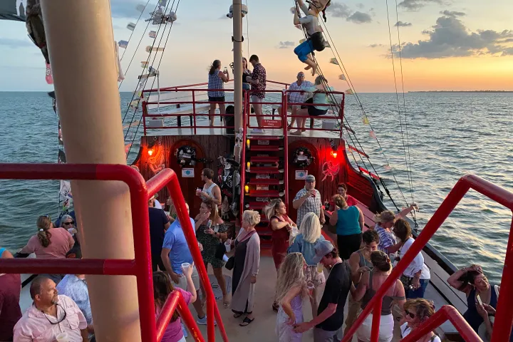 People enjoying a sunset party on a boat with a pirate theme and deck decorations.