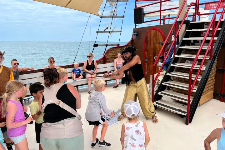 Group of kids on a pirate-themed boat engaged in a game led by a man in a pirate costume.