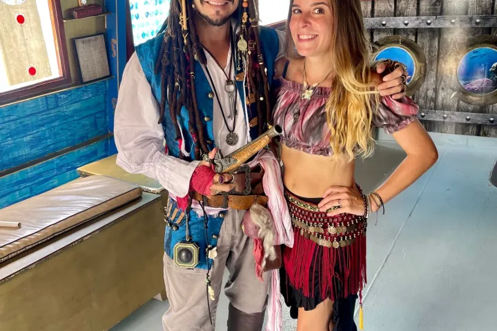 Two people in pirate costumes smiling inside a pirate-themed room.