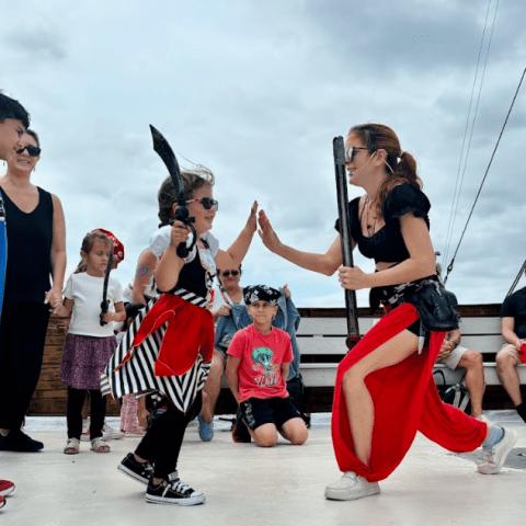 Woman and child dressed as pirates high-fiving on ship deck, with onlookers watching.