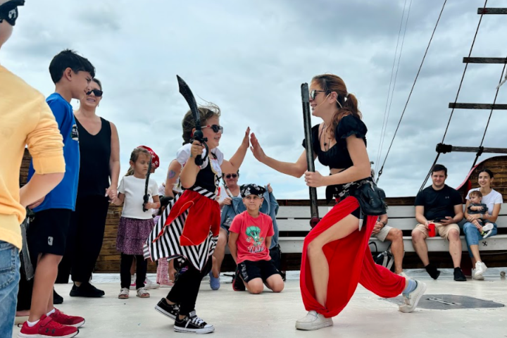 Woman and child dressed as pirates high-fiving on ship deck, with onlookers watching.