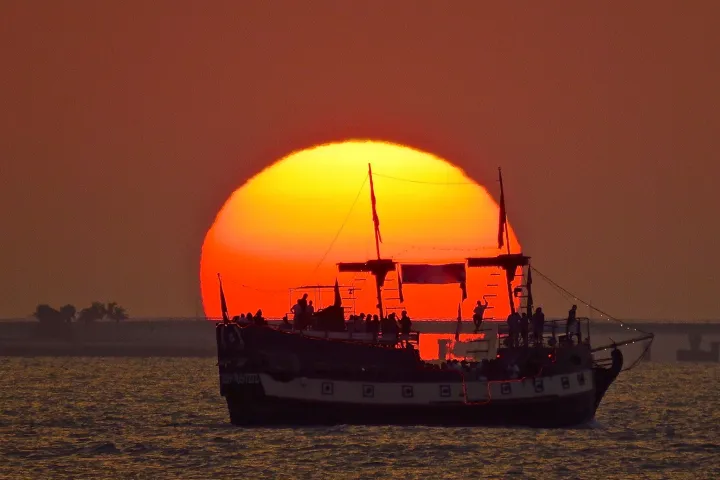 Silhouette of a boat against a vibrant sunset over the water.