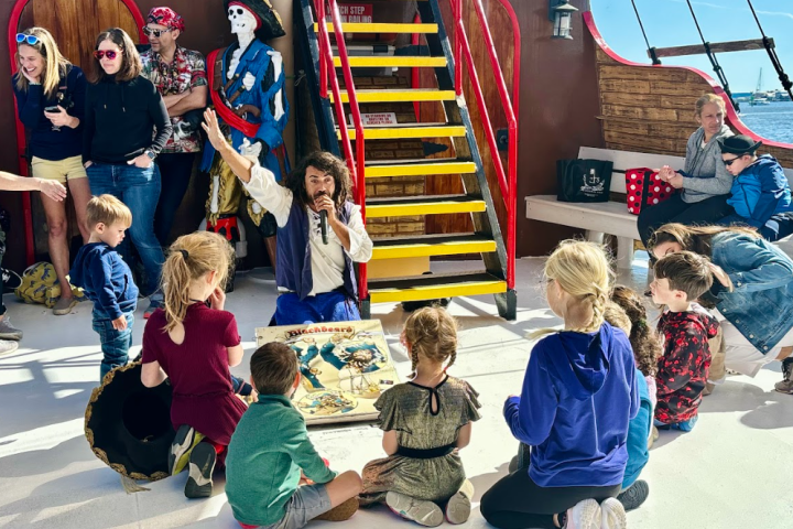 Pirate-themed show on a ship, featuring a performer with microphone, kids and adults watching.