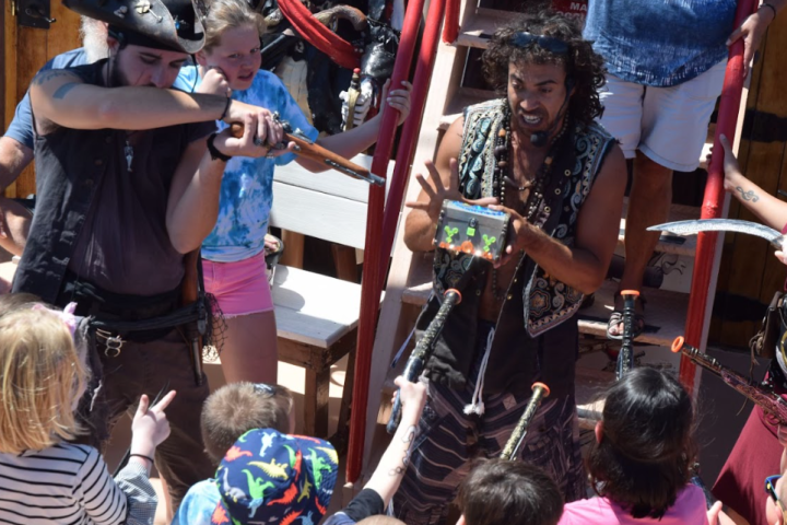 Pirate actors entertaining children with swords on a ship.