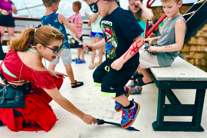 Children in pirate costumes playing on a ship; one holds a toy sword.