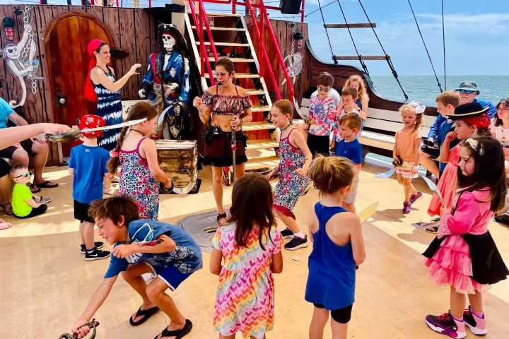 Children play on a pirate-themed ship deck, holding toy swords and wearing costumes.