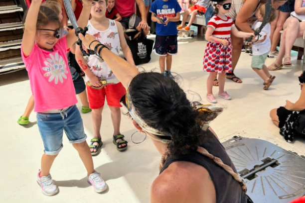 Kids playing a pirate game with an adult on a ship deck, surrounded by other children and adults.