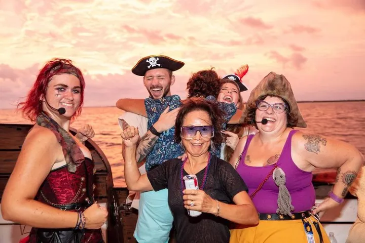 Group of people in pirate costumes smiling on a boat during sunset.