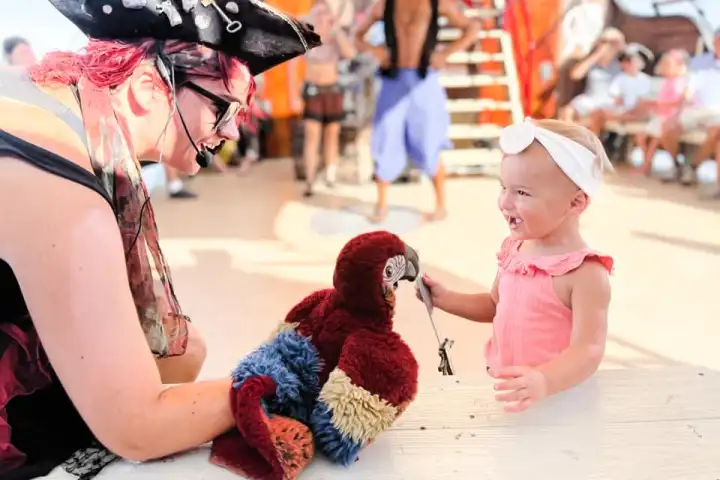 Smiling baby with a pirate hat, touching a parrot puppet.