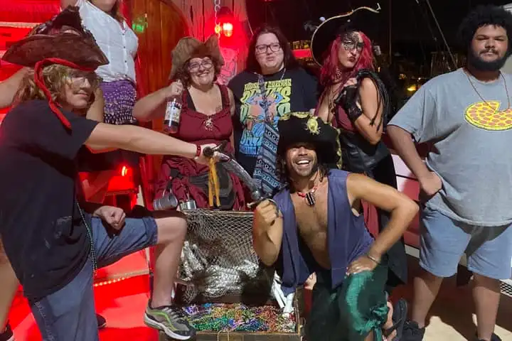 Group in pirate attire posing with treasure chest on a ship at night.