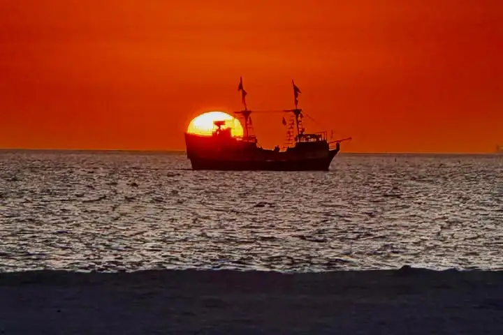 Silhouette of a pirate ship at sunset on the ocean.