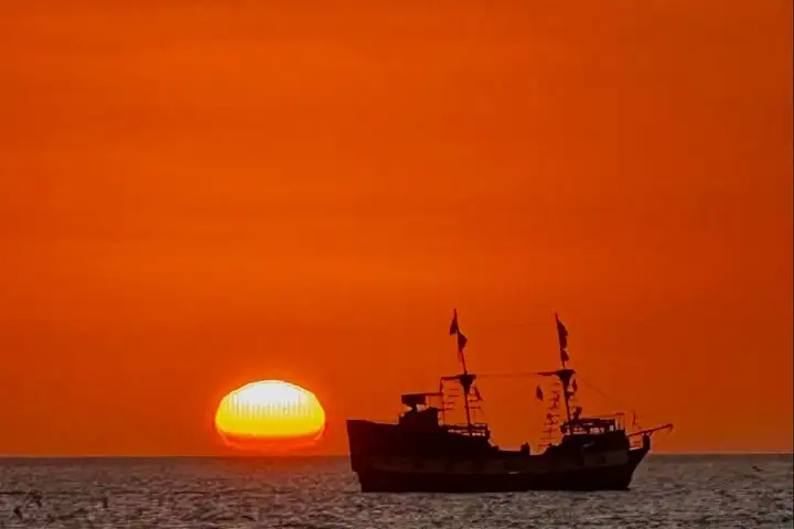 Silhouette of a ship against an orange sunset on the ocean horizon.