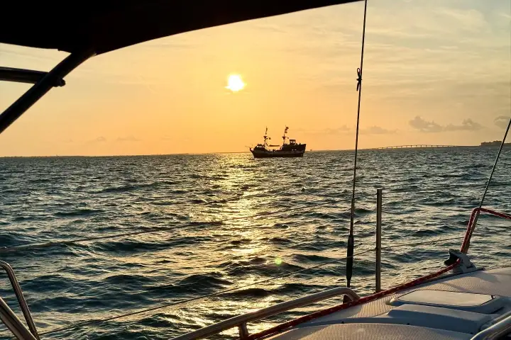 Sunset view from boat deck with pirate ship silhouette on ocean.