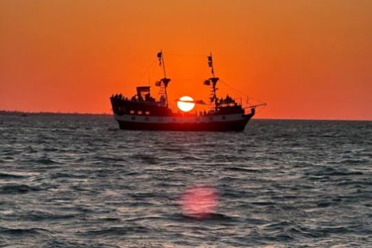 Silhouette of a ship at sunset on the ocean with orange sky.