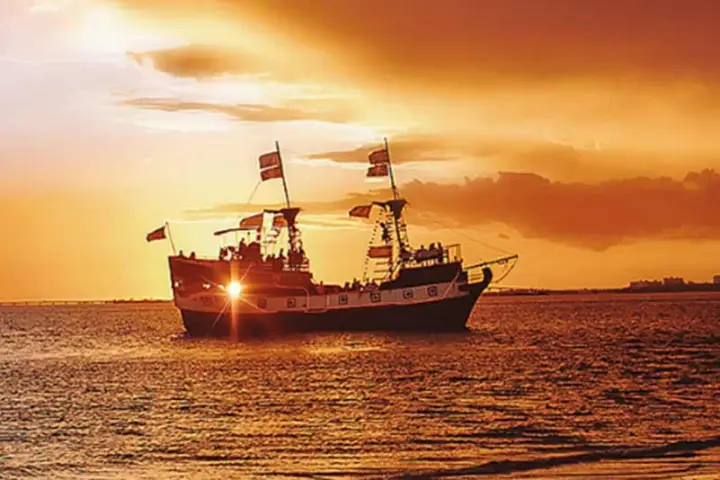 Silhouette of a ship sailing at sunset on calm waters with an orange sky.