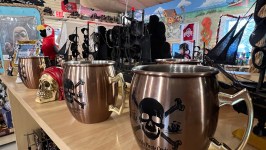 Store shelf with pirate-themed mugs, a parrot figurine, skulls, and model ships.