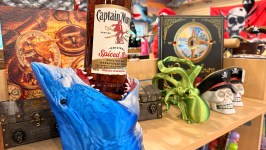 Shelf with pirate-themed items, rum bottle in shark holder, skull, squid, and treasure map book.