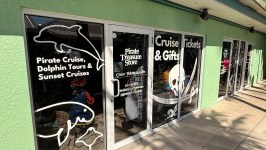Green building exterior with windows advertising pirate and dolphin cruises and gift shop.
