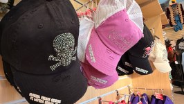 A display of colorful hats with designs, including a rhinestone skull, on a wooden shelf.