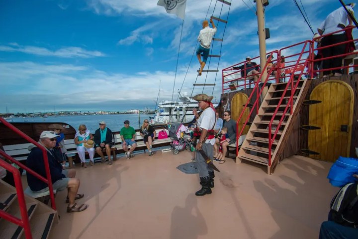 Pirate-themed tour on a boat with people seated; one person climbing mast.