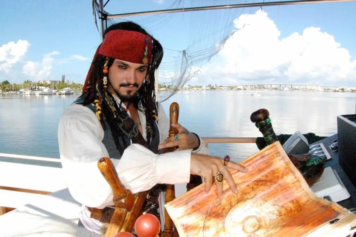 Person in pirate costume with map on boat, calm water background.