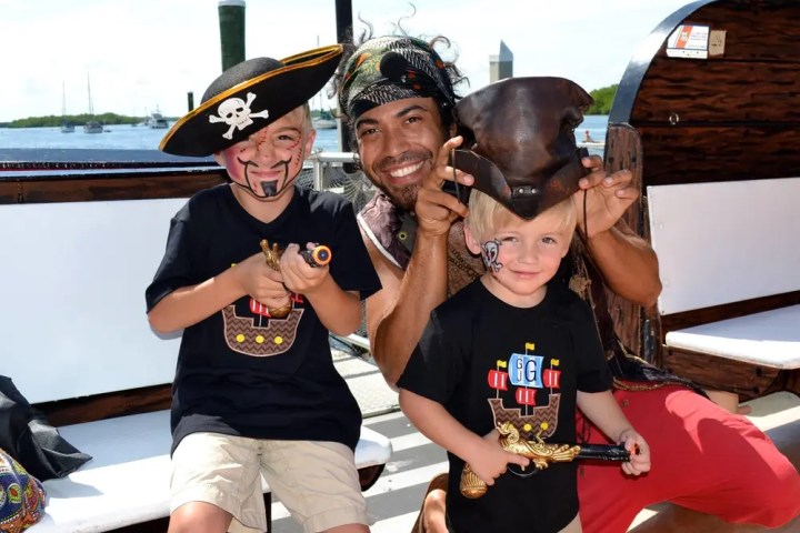 Two children and an adult dressed as pirates on a boat, smiling and holding toy guns.